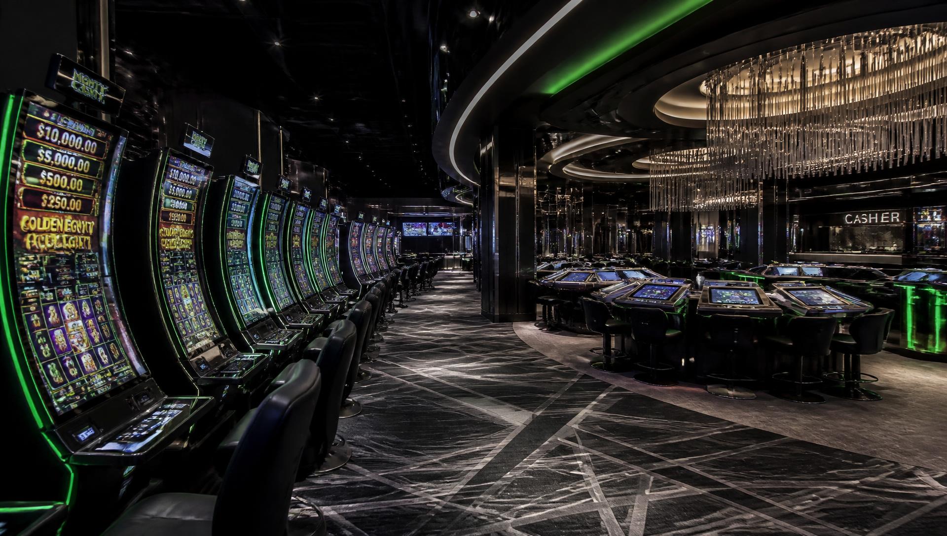 Modern casino gaming floor with rows of slot cabinets and electronic tables